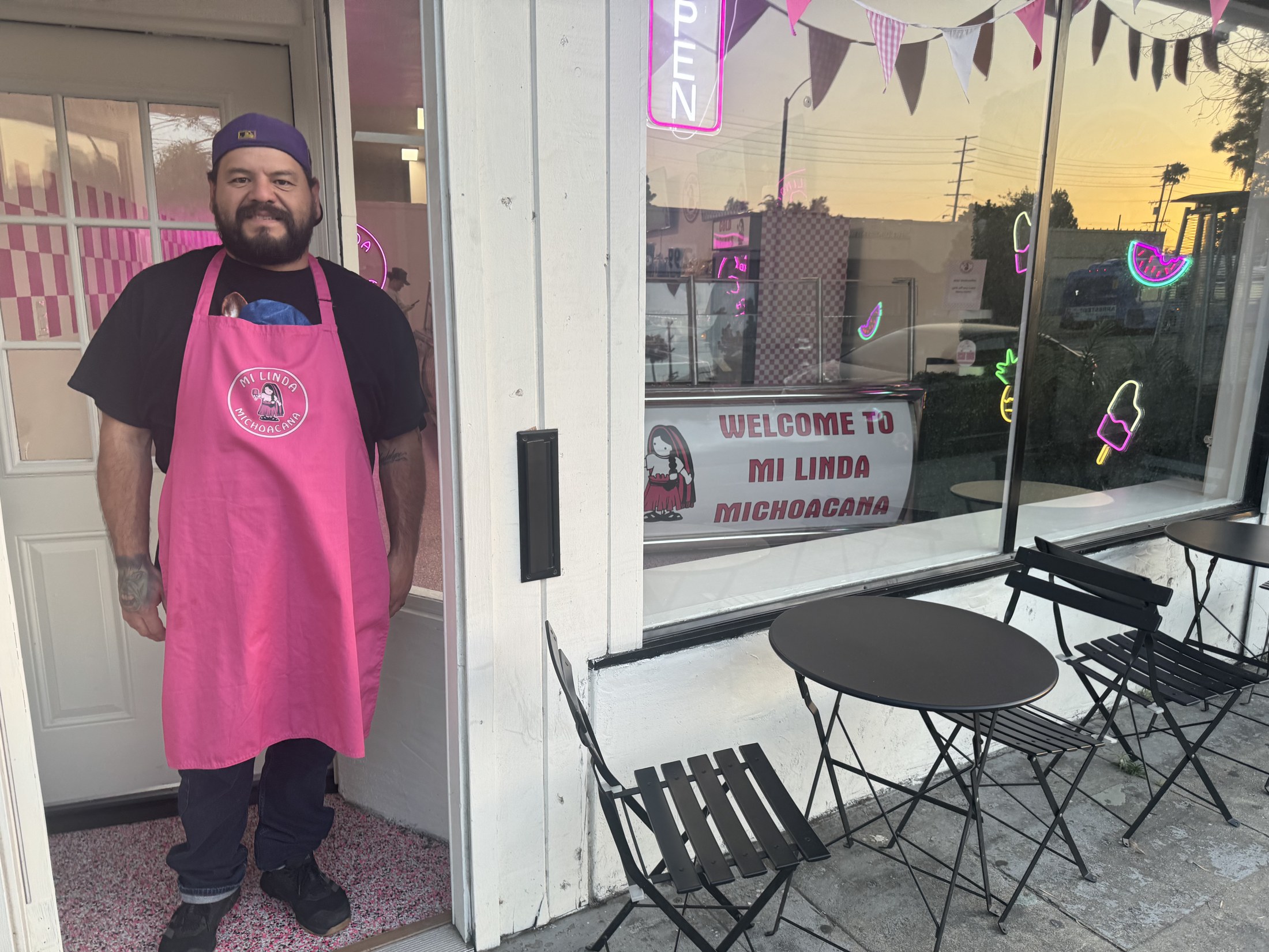 Reuben standing outside the storefront at sunset, with the neon paletas signs glowing in the window